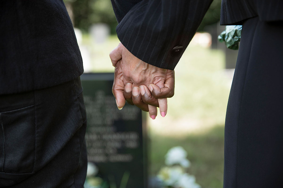 Close up people holding hands by grave loved one.